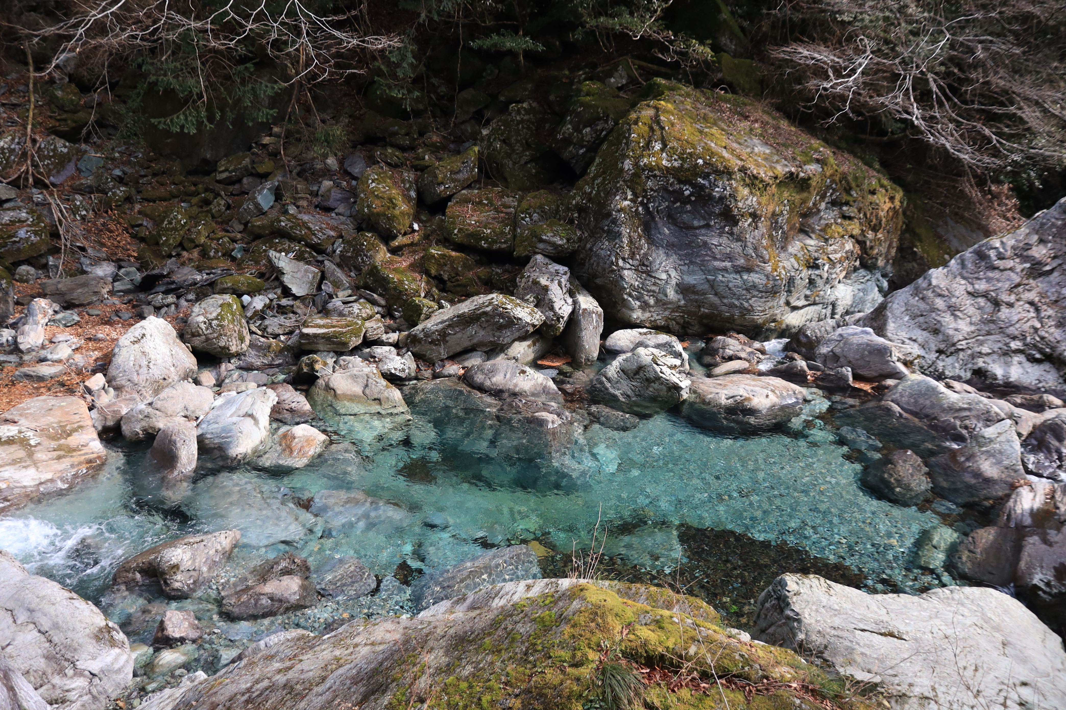 Close-up of the crystal clear turquoise pools at Hiryu Falls surrounded by rocks and moss