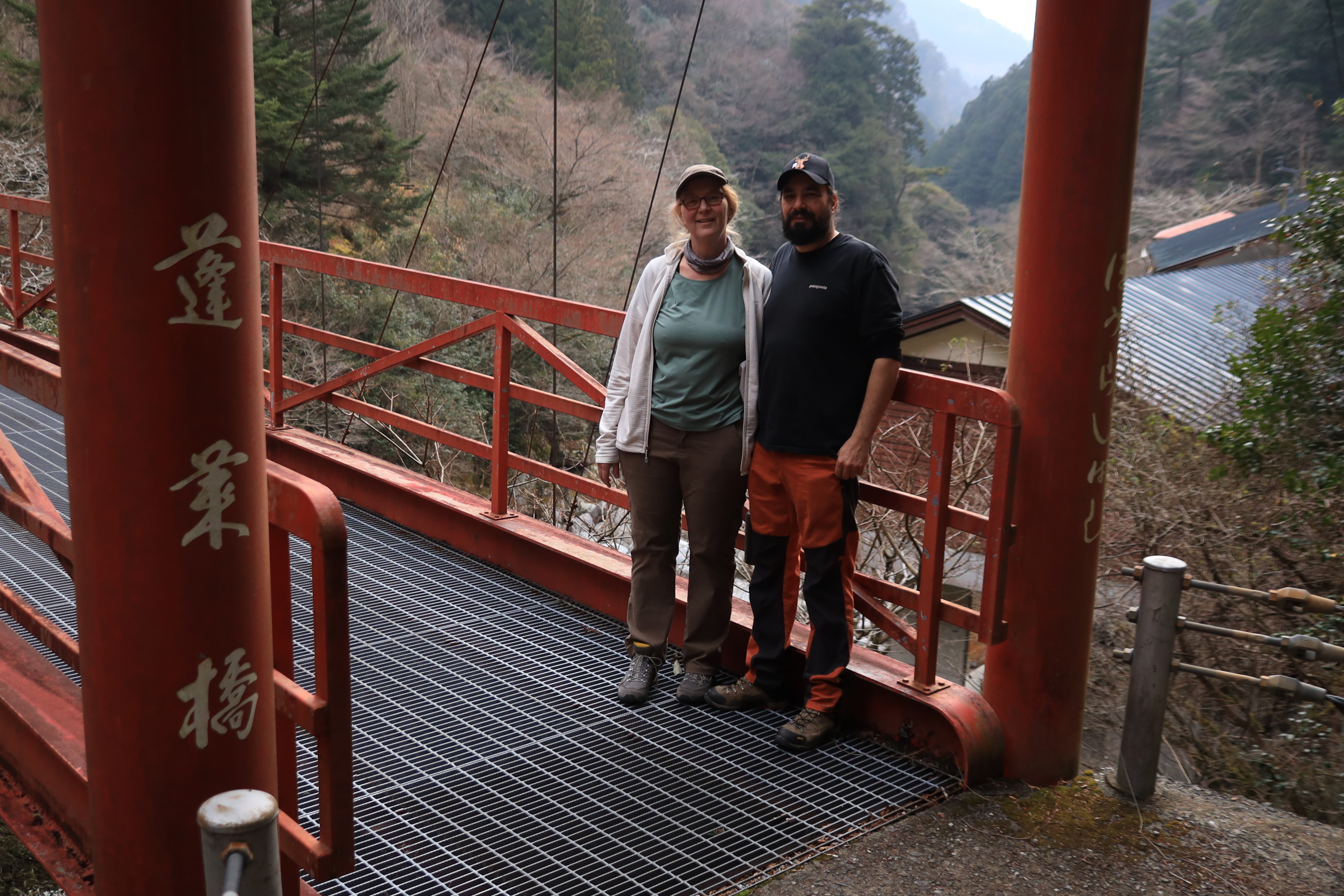 Couple standing on a red bridge at Yasui Valley with mountains in the background