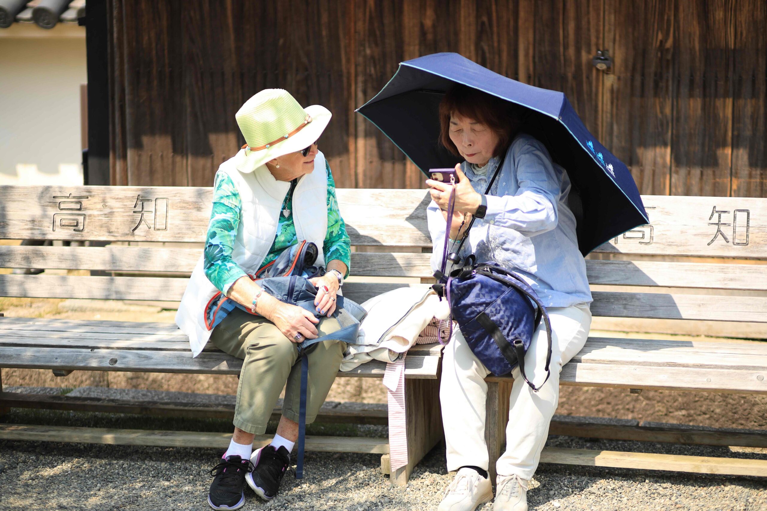 American tourist and local Japanese woman sharing photos on bench at Kochi Castle