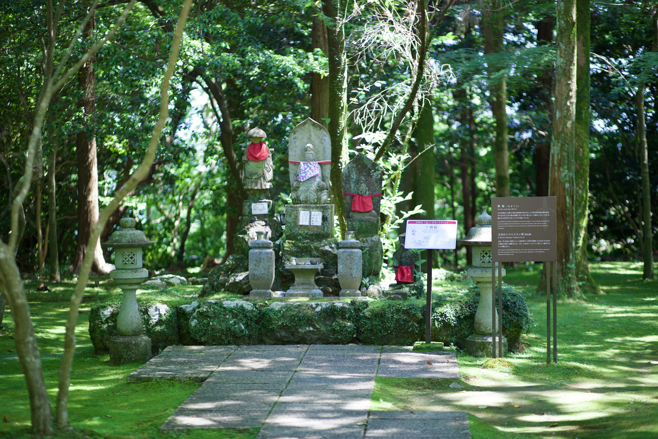 Stone guardian statue dressed in red bib among green moss at Chikurinji Temple