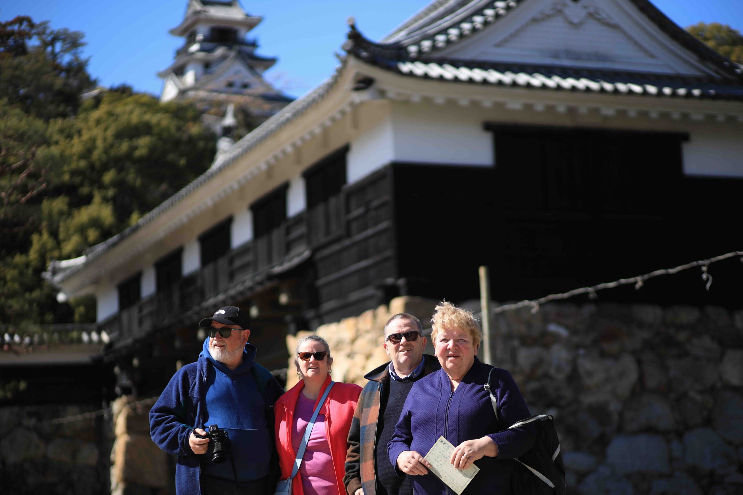 Four tour guests posing in front of Kochi Castle's main gate on a clear day