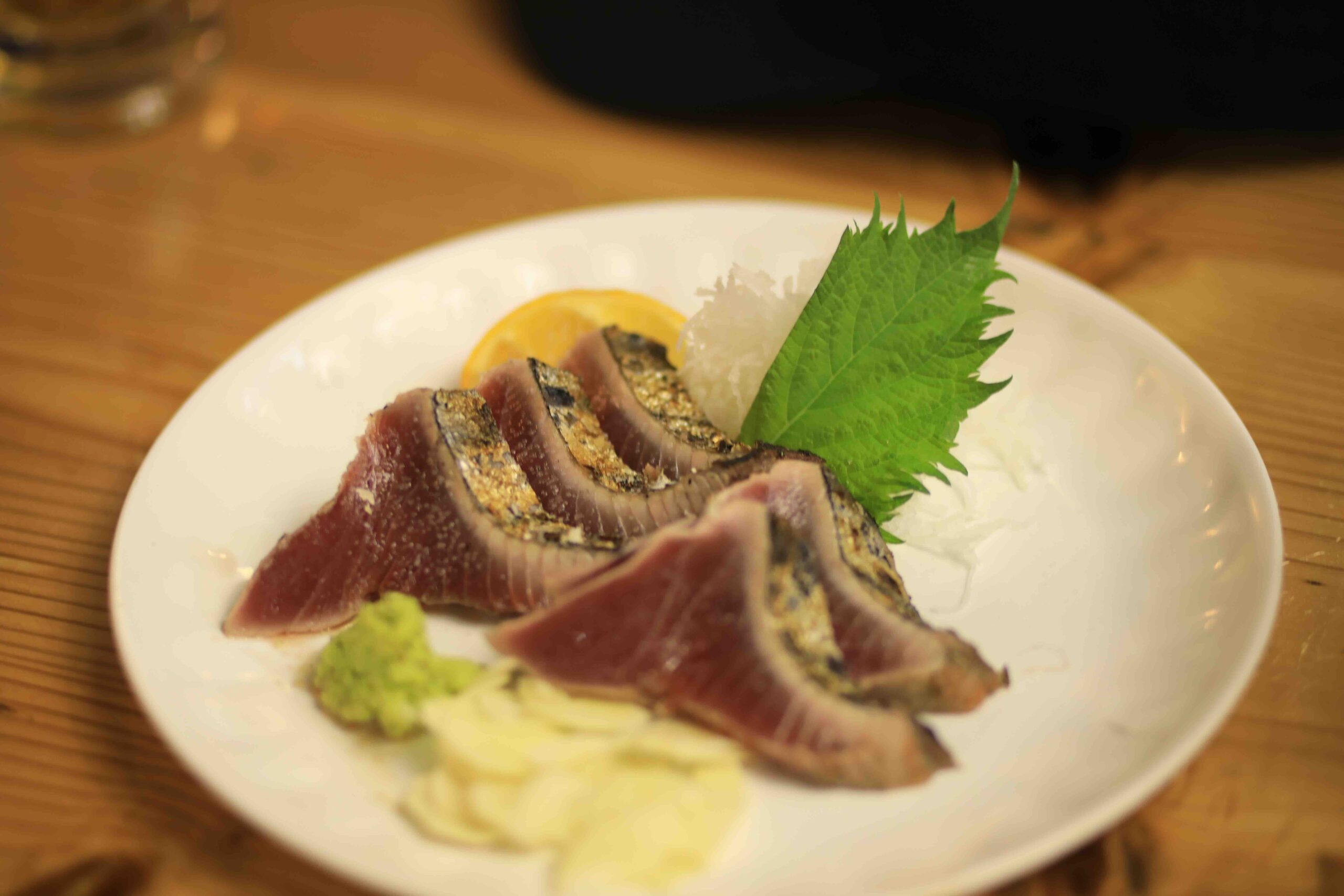 A plate of katsuo no tataki seared bonito with wasabi and garnish at Hirome Market Kochi