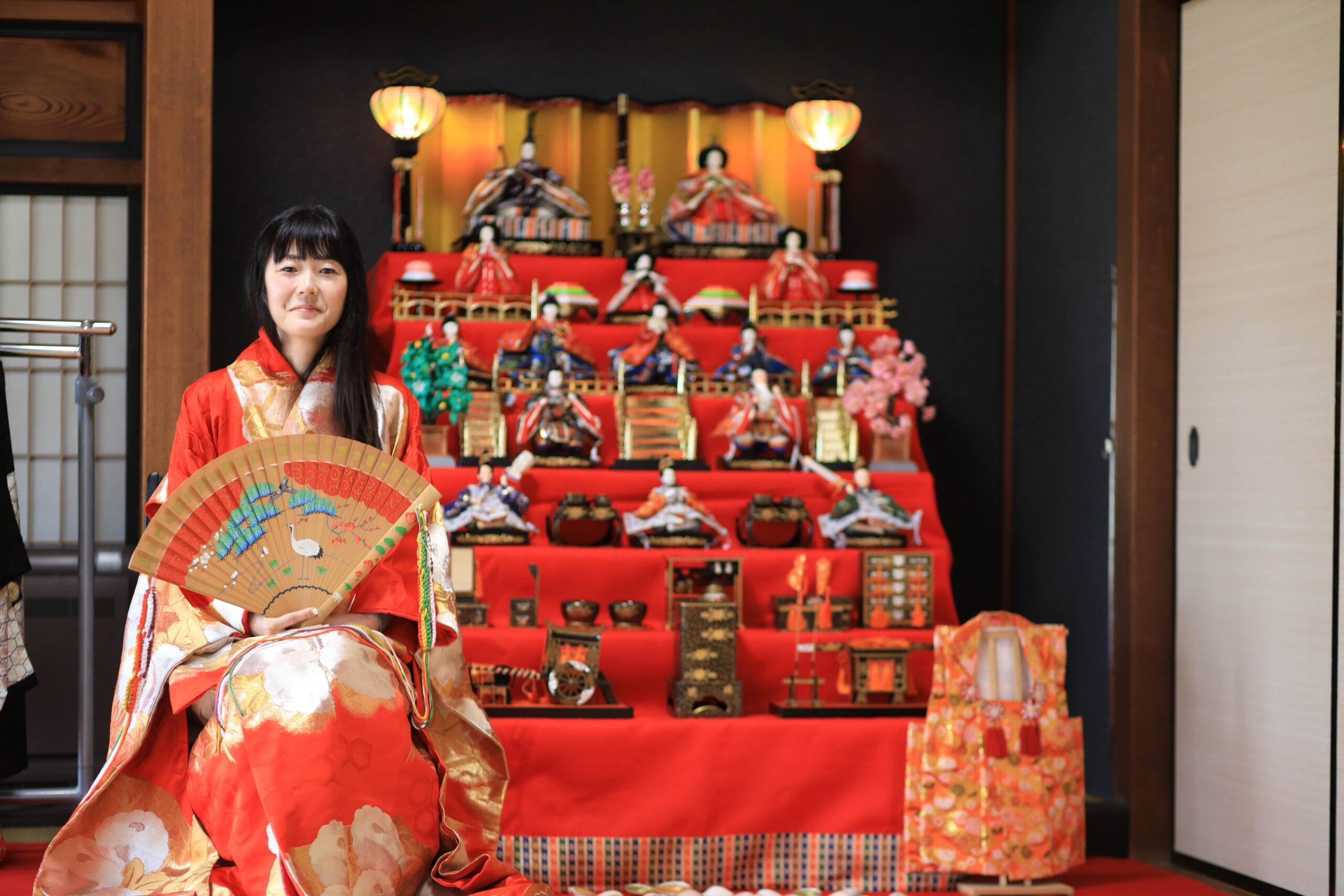 Woman in red kimono sitting in front of a full seven-tier Hina doll display