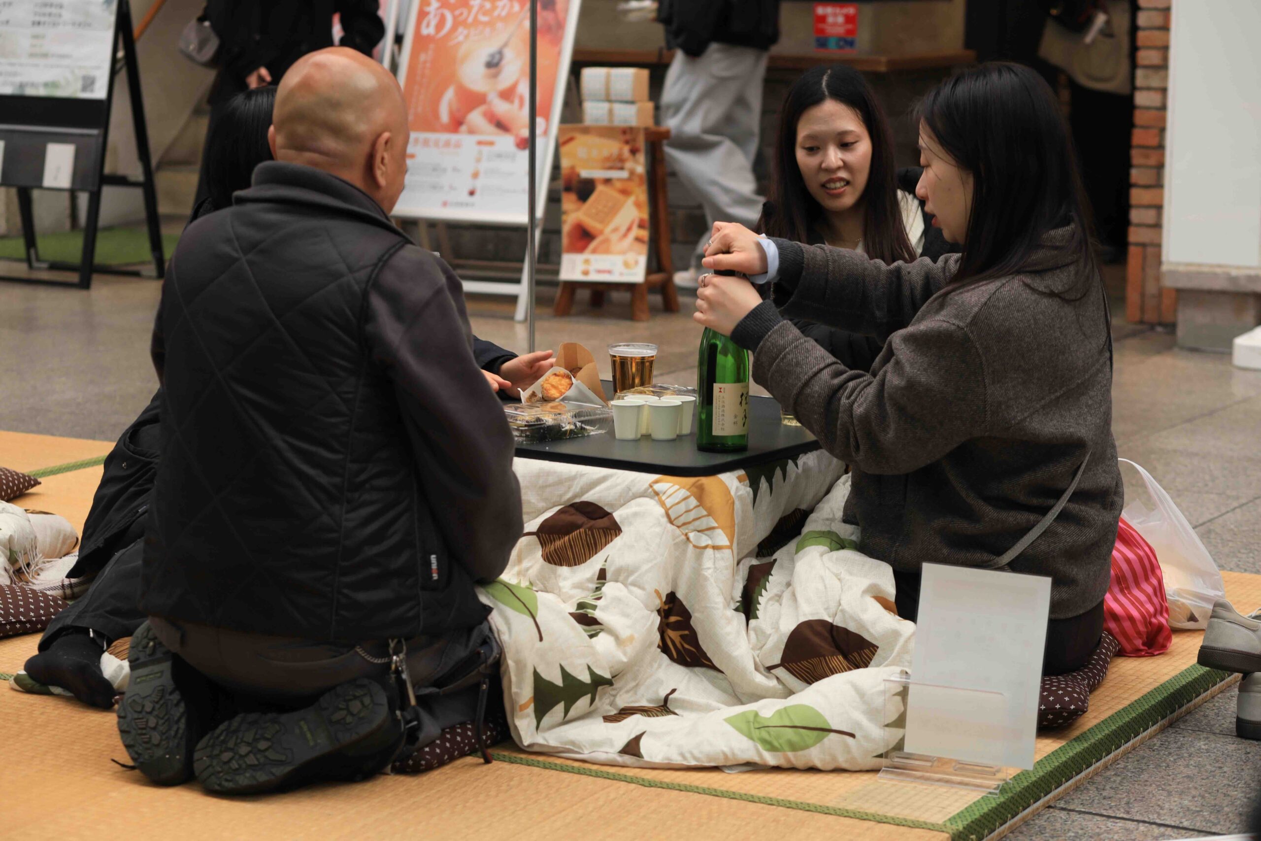 People sitting around a kotatsu table in the arcade drinking sake at Tosa no Okyaku