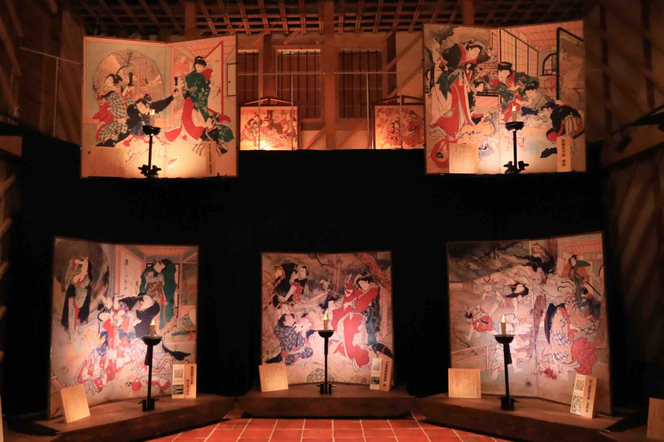 Interior of the Ekin-Gura museum showing multiple large kabuki-themed folding screen paintings displayed in candlelight