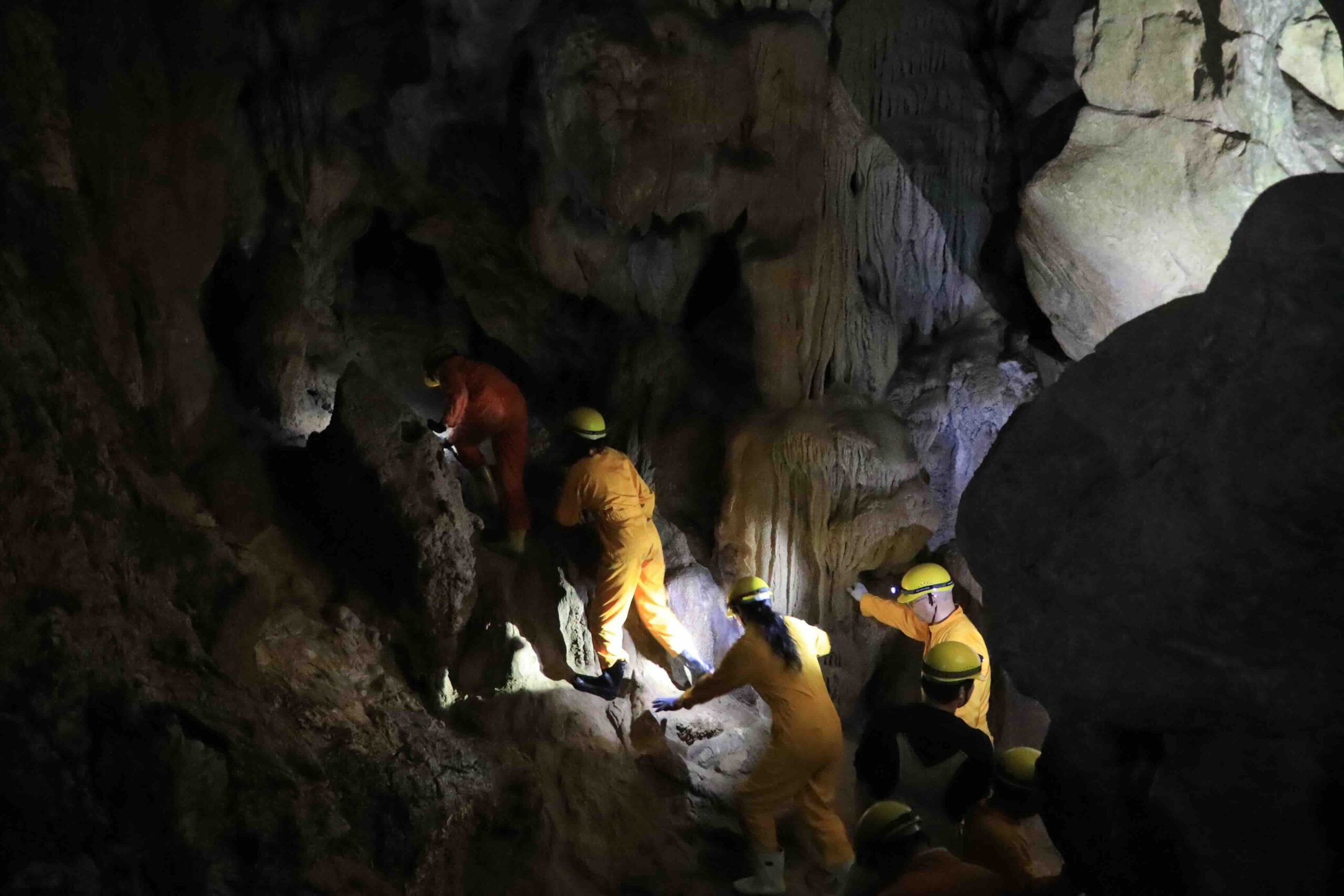 Adventure tour participants in yellow overalls and helmets climbing through wild sections of Ryugado cave Kochi