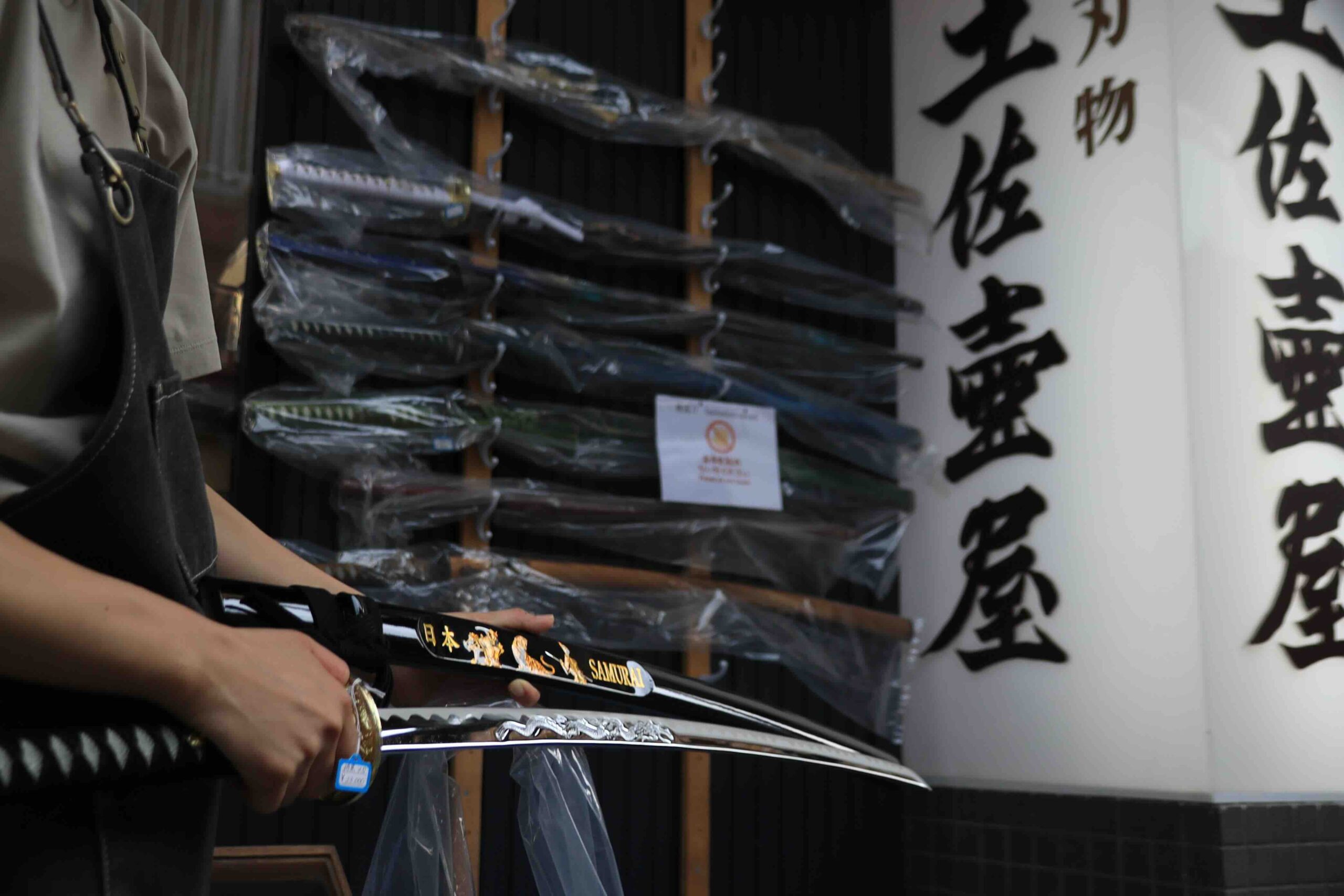 Shop staff holding a decorative samurai sword at a traditional Tosa forged blade shop near Ryugado Kochi