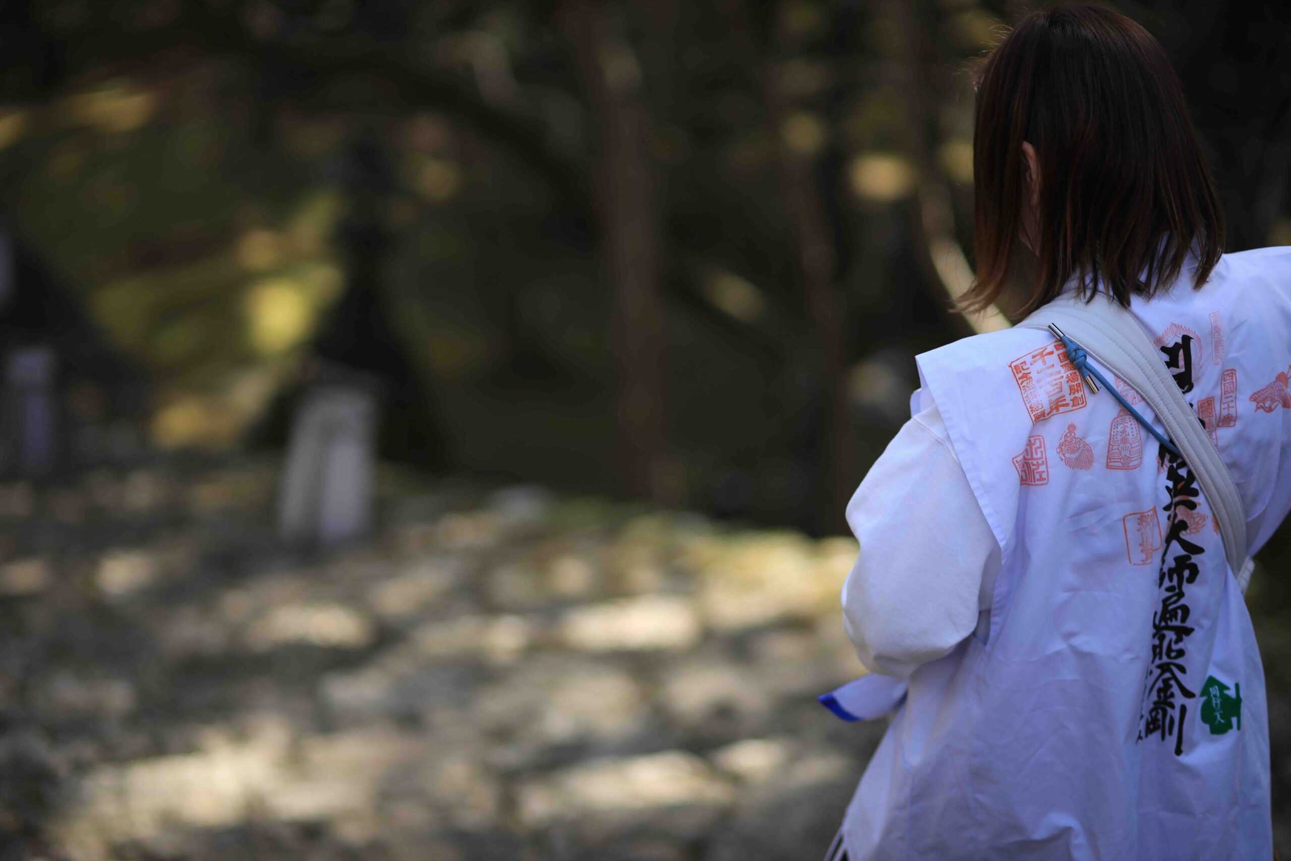 A pilgrim in a white jacket covered with red temple stamps walking through Chikurinji Temple grounds