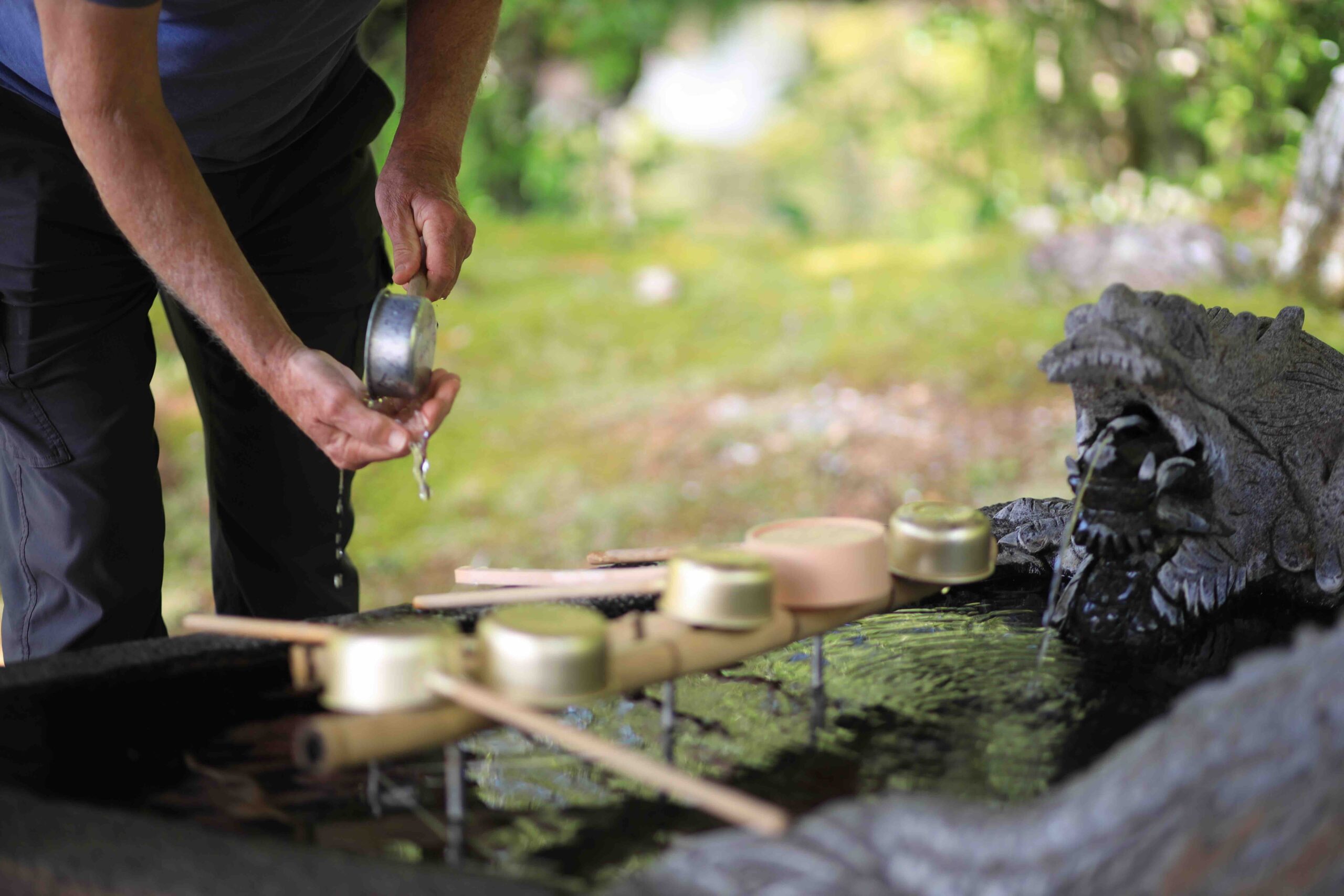 Visitor performing the hand-washing ritual at the stone water basin at a Japanese temple