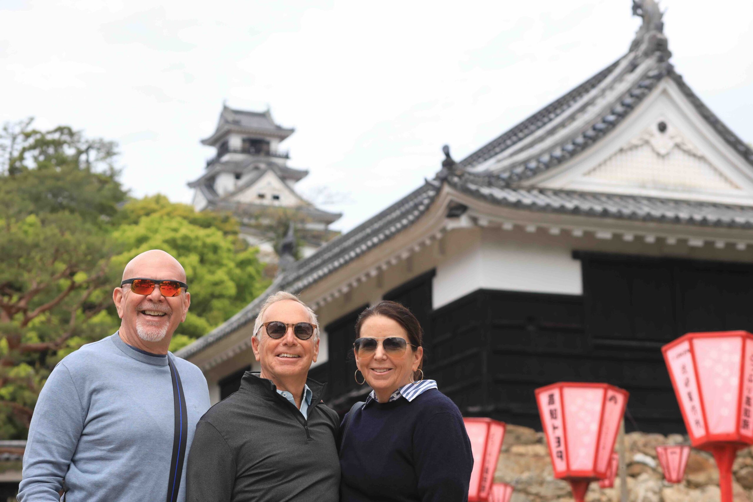 Three guests smiling in front of Kochi Castle with red lanterns