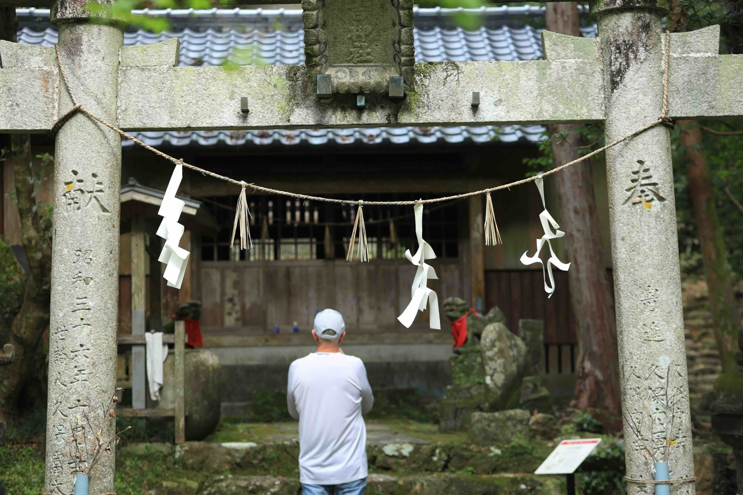 A visitor praying quietly at a small torii gate shrine within Chikurinji Temple grounds
