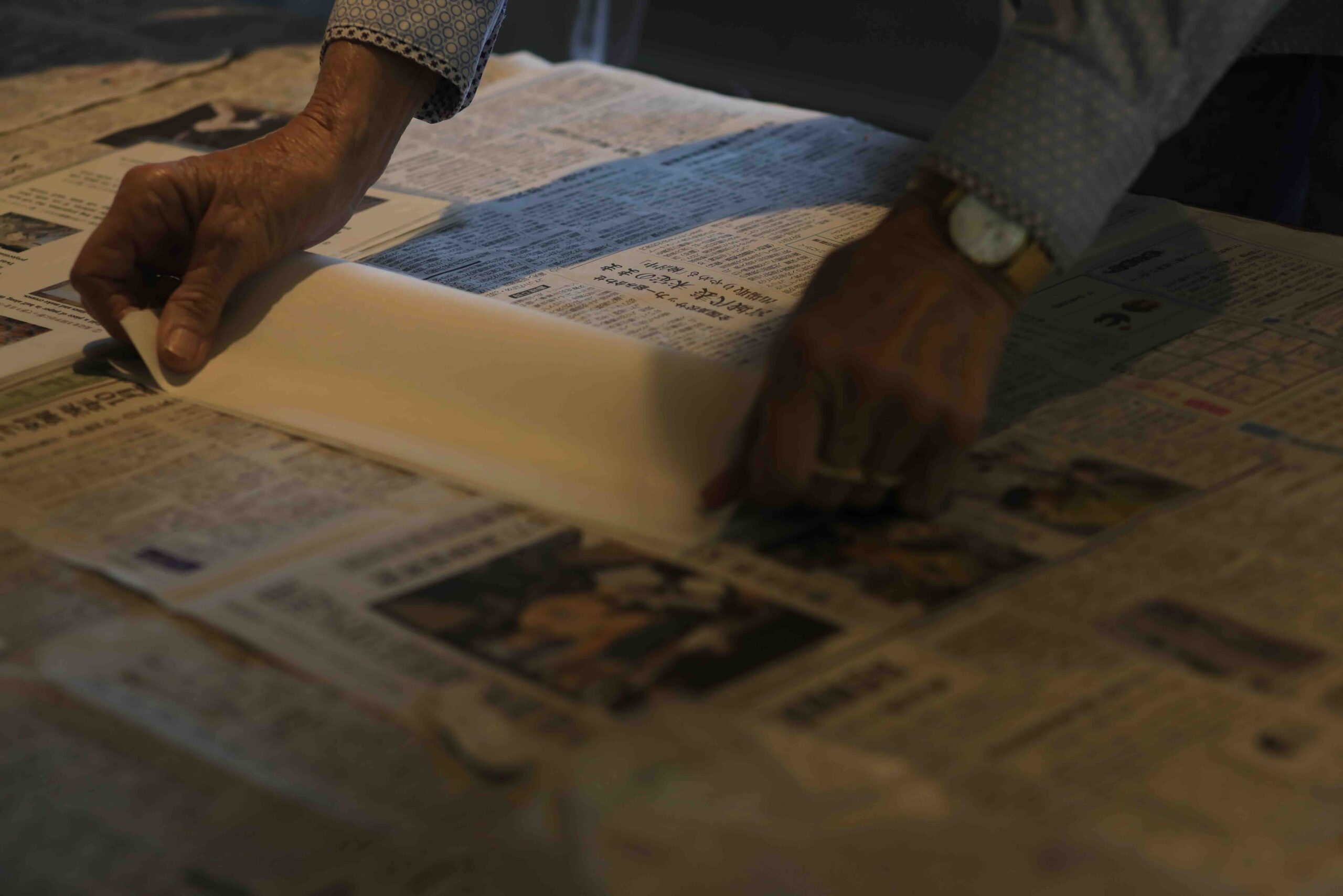 Hands carefully placing washi paper onto a bamboo uchiwa fan frame during a traditional fan-making workshop in Ino Town, Kochi