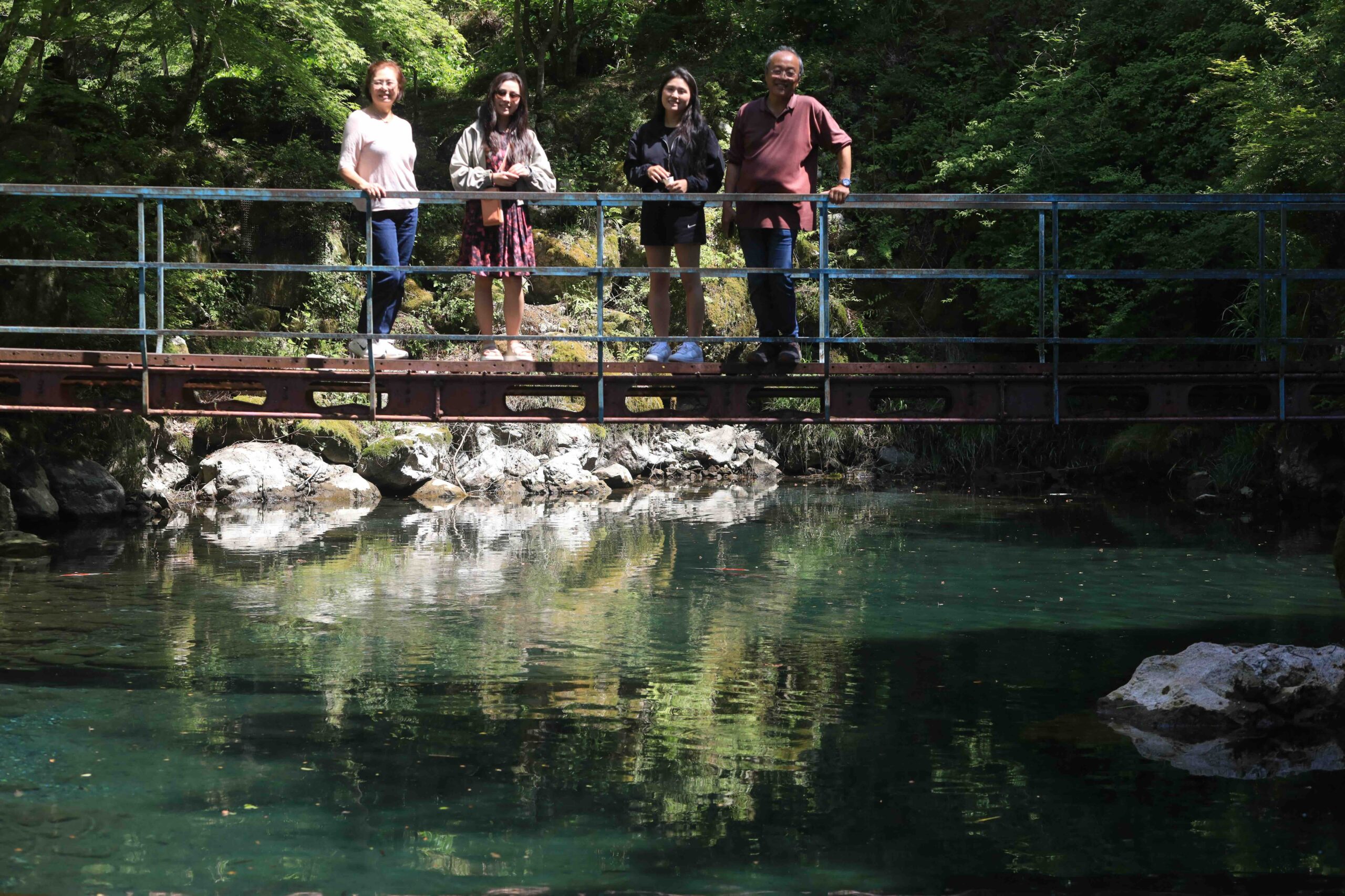 Family on bridge over crystal clear blue green water in Tsuno-cho Kochi Japan